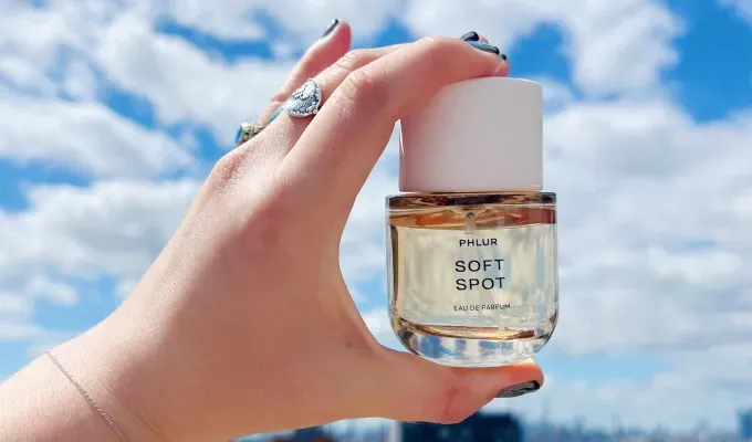 phlur-fragrance-review: A white hand adorned with rings and painted nails holds up a skin-tone color full-sized bottle of perfume. It’s label says Soft Spot. Original photo.' title='I Tried All 22 Phlur Fragrances and Here’s How I’m Ranking Them (with Original Photos)