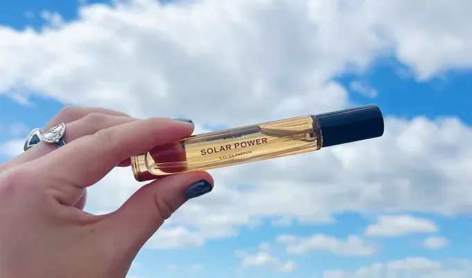 phlur-fragrance-review: A white hand adorned with rings and painted nails holds up a light yellow travel-sized bottle of perfume. It’s label says Solar Power. Original photo.' title='I Tried All 22 Phlur Fragrances and Here’s How I’m Ranking Them (with Original Photos)