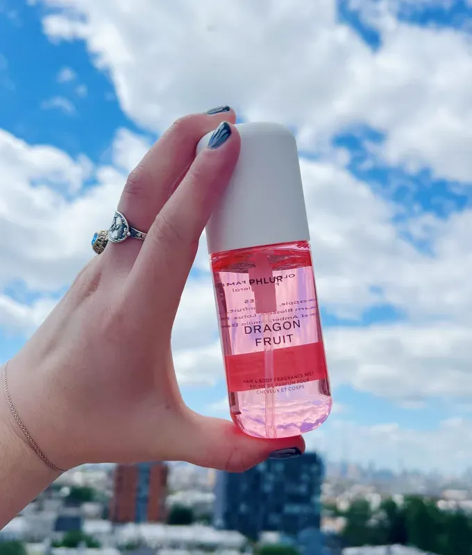 phlur-fragrance-review: A white hand adorned with rings and painted nails holds up a pink travel-sized bottle of body mist. It’s label says Dragon Fruit. Original photo.' title='I Tried All 22 Phlur Fragrances and Here’s How I’m Ranking Them (with Original Photos)