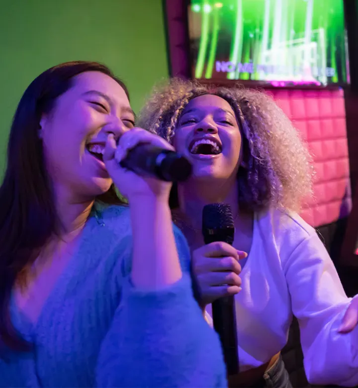 karaoke songs: two friends sing together in a dark room' fetchpriority='high' title='75 Easy Karaoke Songs That Will Bring Down the House