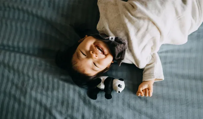 baby-names-that-mean-miracle: A young Asian baby girl lays on a blue sheet and smiles at the camera. There’s a panda plushie next to his head.' fetchpriority='auto' title='50 Baby Names That Mean Miracle