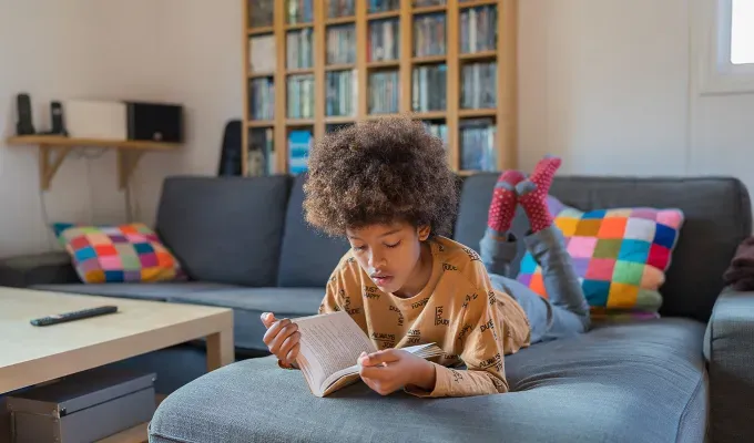 realistic-daily-schedules-for-kids: a young boy laying on a couch and reading' fetchpriority='auto' title='5 Realistic Daily Schedules for Kids From Ages 0 to 11 According to Experts