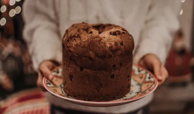 Italian Christmas Traditions - A person in a white sweater holds a large brown baked good. There’s a blurry holiday scene behind them.' fetchpriority='auto' title='13 Classic Italian Christmas Traditions to Try in 2024