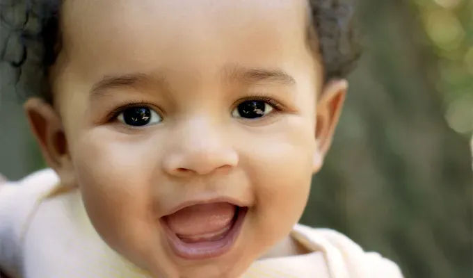 names-that-mean-summer: A close up photo of a young baby of color smiling at the camera. He has curly brown hair.' fetchpriority='auto' title='60 Names That Mean Summer to Celebrate Your Baby’s Sunny Spirit