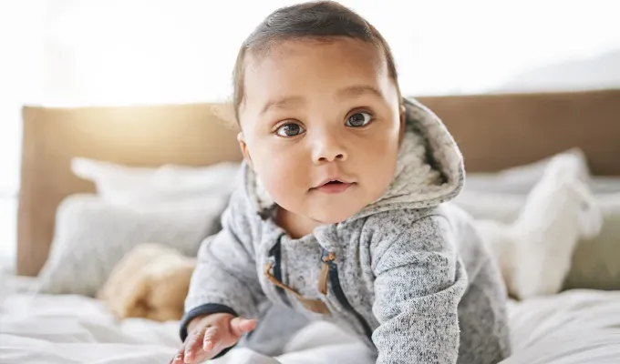 uncommon baby names: baby wearing a hoodie crawls on a bed' fetchpriority='auto' title='150 Uncommon Baby Names to Help Your Child Stand Out from the Crowd