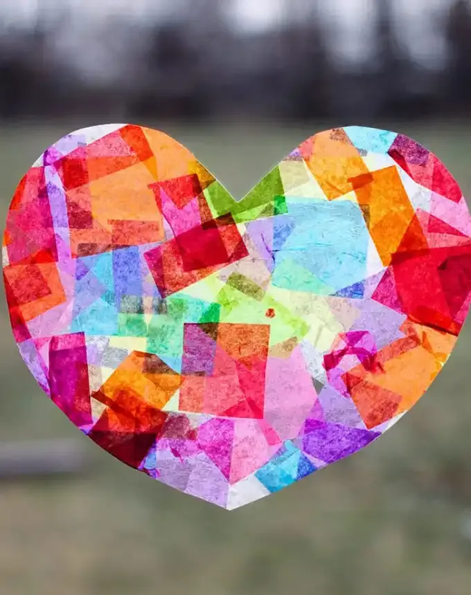 52 Fun and Easy Valentine’s Day Crafts for Kids - A white tissue heart covered in other colorful tissue is used as a sunctacher on a window.' title='70 Fun and Easy Valentine’s Day Crafts for Kids
