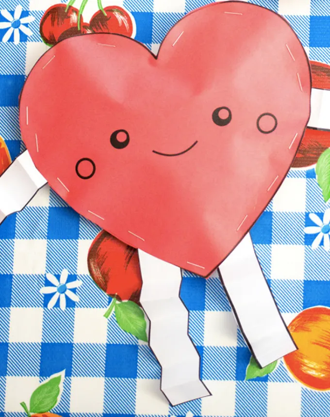 52 Fun and Easy Valentine’s Day Crafts for Kids - A stuffed red heart with a smile arms and legs sits on a blue and white check background that also features some fruit designs.' title='70 Fun and Easy Valentine’s Day Crafts for Kids