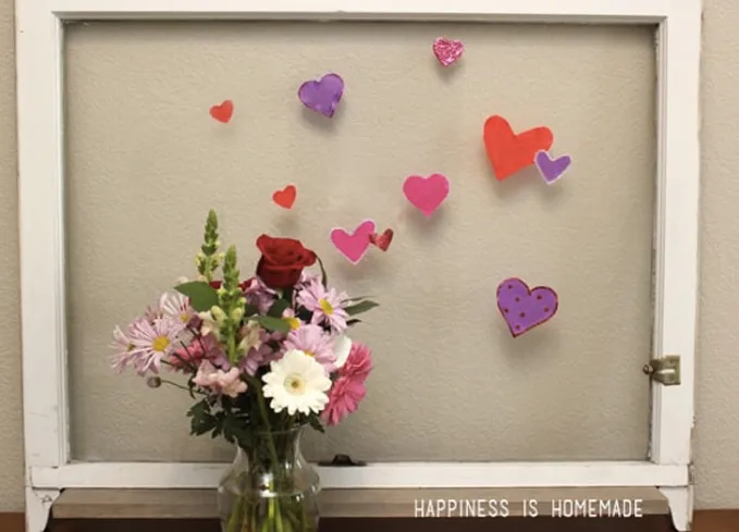 52 Fun and Easy Valentine’s Day Crafts for Kids - A glass window with a white border features red pink and purple heart-shaped window clings. In front of it is a small bouquet of flowers.' title='70 Fun and Easy Valentine’s Day Crafts for Kids
