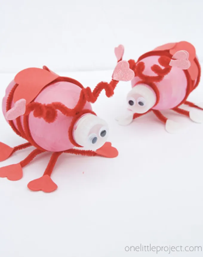 52 Fun and Easy Valentine’s Day Crafts for Kids - Two small water bottles are decorated in pink and red paper pipe cleaners and googly eyes to resemble cartoonish love bugs.' title='70 Fun and Easy Valentine’s Day Crafts for Kids
