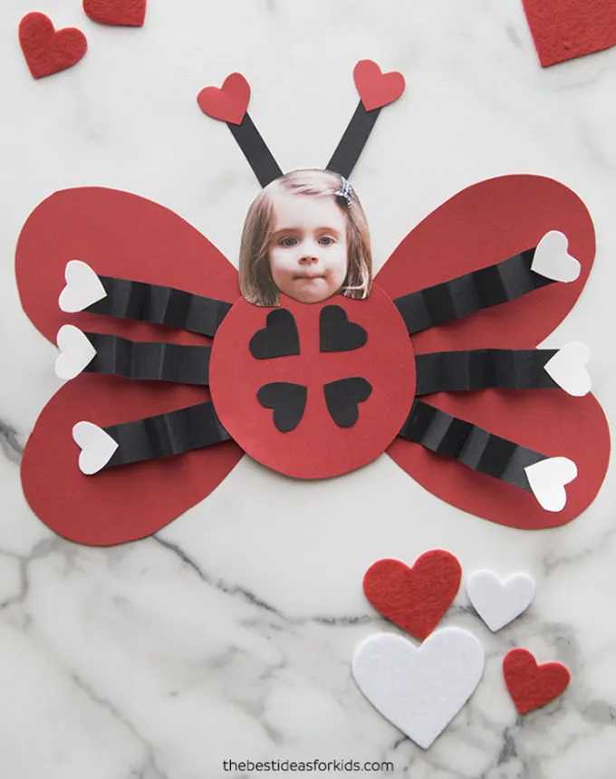 52 Fun and Easy Valentine’s Day Crafts for Kids - A red paper craft in the shape of a lady bug. A photo of a child’s head is where the ladybug’s should be. The child’s photo is affixed with antennas.' title='70 Fun and Easy Valentine’s Day Crafts for Kids