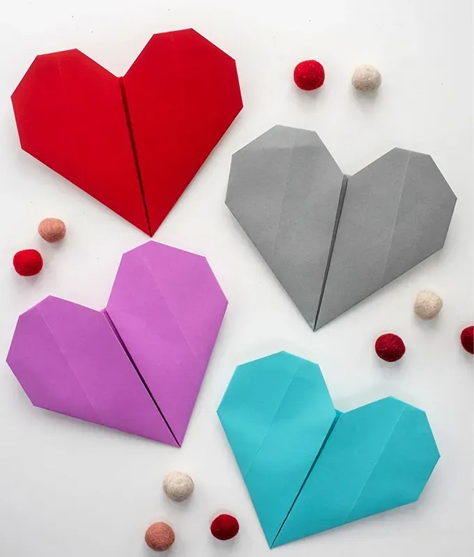 52 Fun and Easy Valentine’s Day Crafts for Kids - Origami hearts in red purple gray and blue lay on a white surface. There are decorative red and white beads that rest on the surface as well.' fetchpriority='auto' title='70 Fun and Easy Valentine’s Day Crafts for Kids