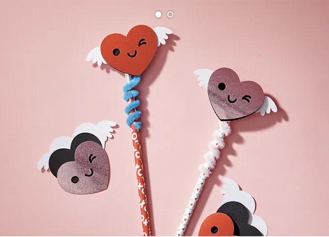 52 Fun and Easy Valentine’s Day Crafts for Kids - Valentine’s themed pencils topped with paper craft pencil toppers shaped like hearts with wings. They have smiley faces. All on a light pink background.' title='70 Fun and Easy Valentine’s Day Crafts for Kids