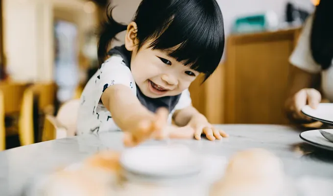 A toddler girl with a mystical and magical name reaching for bread in a restaurant' fetchpriority='auto' title='50 Mystical and Magical Baby Names That Will Put You Under a Spell