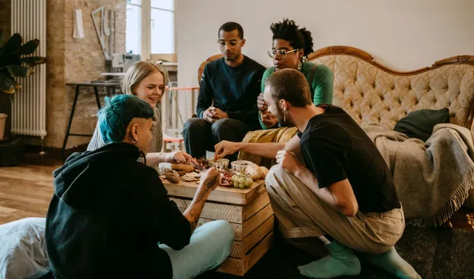 gen-z-slang-terms: A group of young friends sitting in a living room eating a charcuterie board.' fetchpriority='auto' title='From ‘Basic’ to ‘Boujee’ Here Are 29 Gen Z Slang Terms To Keep in Your Back Pocket