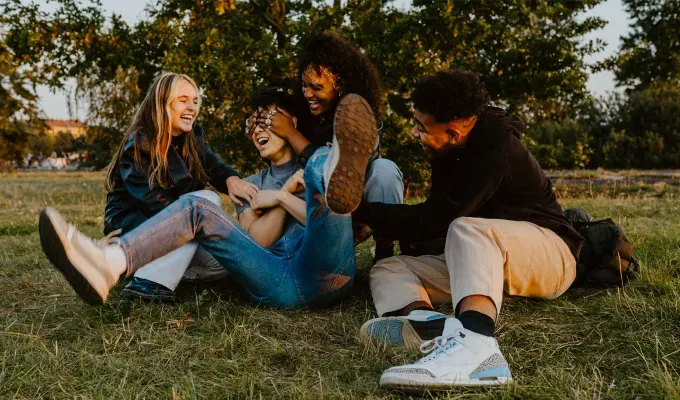 gen-z-slang-terms: A group of young people sitting and laughing together in a grassy spot.' fetchpriority='auto' title='From ‘Basic’ to ‘Boujee’ Here Are 29 Gen Z Slang Terms To Keep in Your Back Pocket