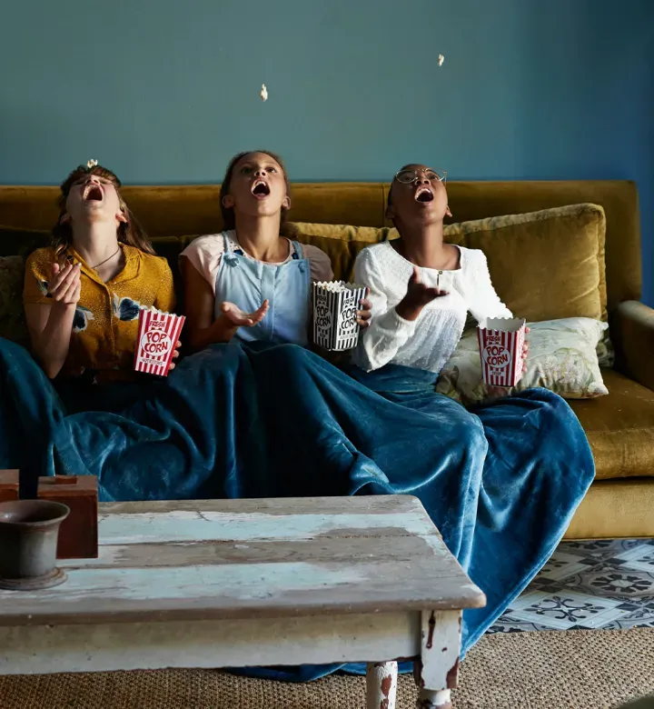 best-tv-shows-for-9-12-year-olds: tween girls watching tv and eating popcorn' fetchpriority='high' title='The 20 Best TV Shows for 9 to 12 Year Olds (Because Your Tween Needs Some Quality Content)