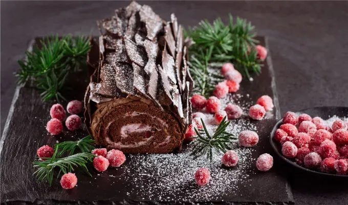 french christmas traditions-A chocolate Bûche de Noël dessert decorated with greenery and berries sits on a table.' fetchpriority='auto' title='15 French Christmas Traditions That Are Oh-So Charming