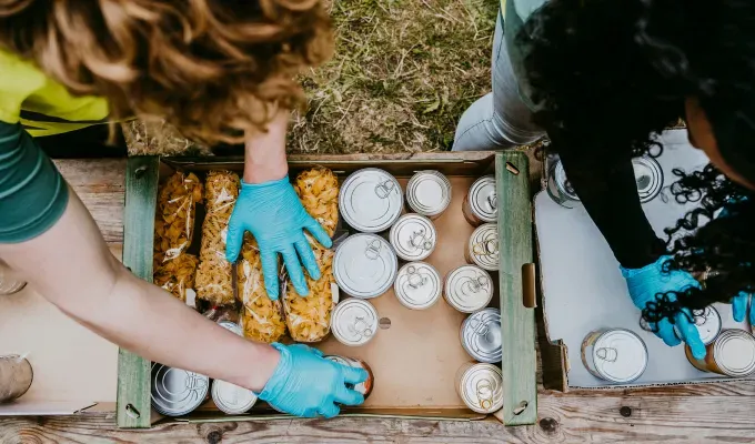 Where to Volunteer on Thanksgiving - An overhead shot of a man and a woman wearing gloves handling boxes filled with cans of food.' fetchpriority='auto' title='Where to Volunteer on Thanksgiving 2024 from Meals on Wheels to Park Clean-Ups
