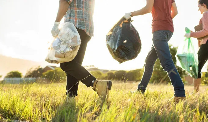 Where to Volunteer for Thanksgiving - Three people with full trash bags walk across a sunny green field.' fetchpriority='auto' title='Where to Volunteer on Thanksgiving 2024 from Meals on Wheels to Park Clean-Ups