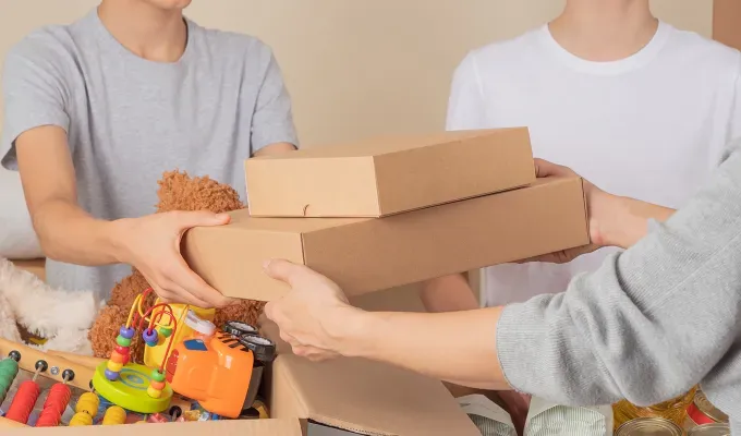 where-to-volunteer-on-thanksgiving: three people exchanging gift boxes filled with toys.' title='Where to Volunteer on Thanksgiving 2024 from Meals on Wheels to Park Clean-Ups