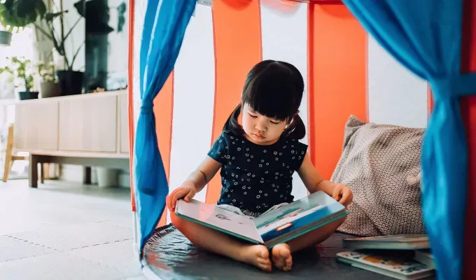 Adorable little girl enjoying herself and spending leisure time at home. She is reading book with her teddy bear in a tent at home' fetchpriority='auto' title='100 Baby Names That Mean Star