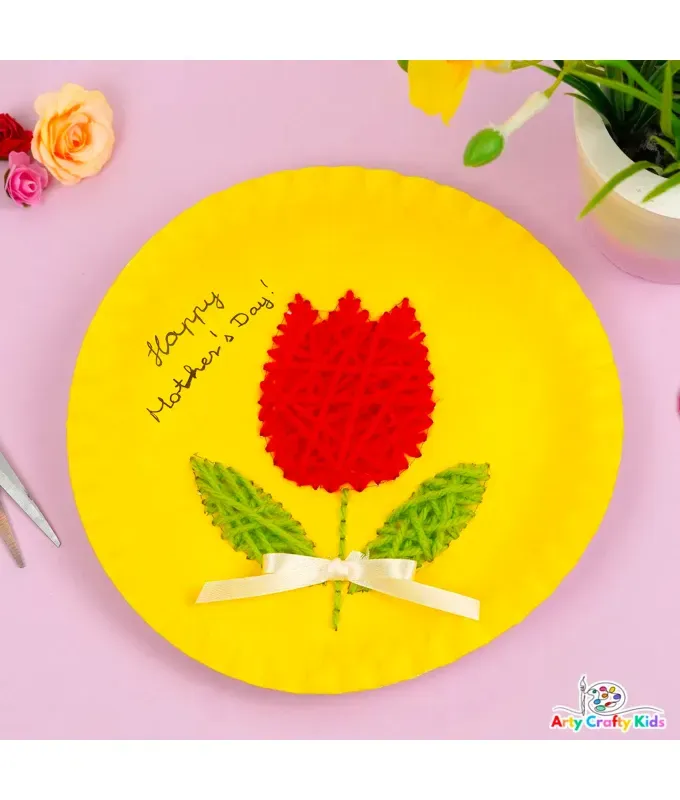 mothers-day-crafts: A yellow paper plate with a red tulip design sewn in yarn in front of a pink background.' title='45 Mother’s Day Crafts for Kids That She’ll Actually Want to Keep