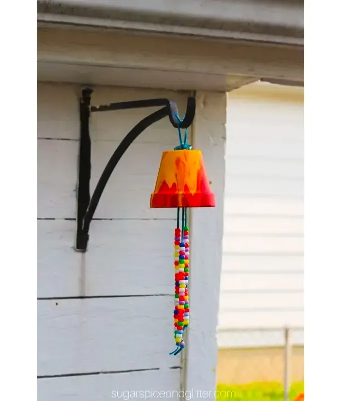 mothers-day-crafts: An upside down flower pot hangs from the side of a house. It has a drippy paint design and beads dangling from it.' title='45 Mother’s Day Crafts for Kids That She’ll Actually Want to Keep