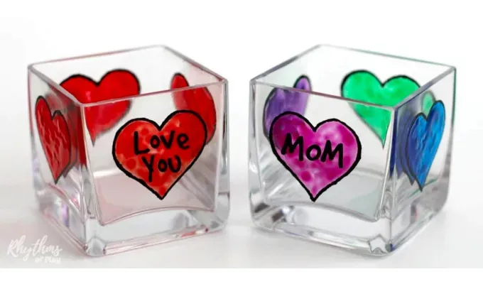 mothers-day-crafts: Two glass candle holders with glass paint decorations on them in the shape of hearts with words like ’Mom’ and ’I love you’ on them.' title='45 Mother’s Day Crafts for Kids That She’ll Actually Want to Keep
