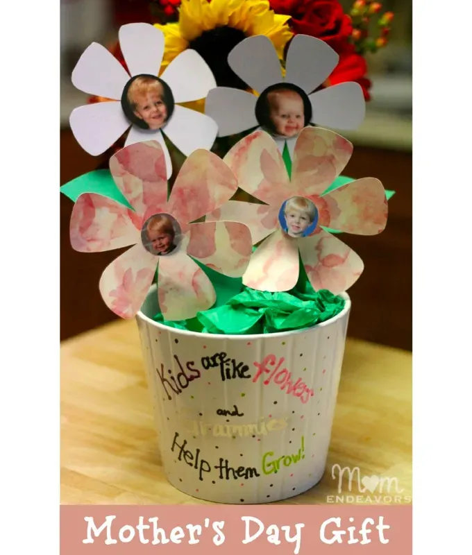 mothers-day-crafts: A white glass flower pot with colorful paper flowers in it. The center of each flower has a photo of a child in it. It sits on a wooden table.' title='45 Mother’s Day Crafts for Kids That She’ll Actually Want to Keep
