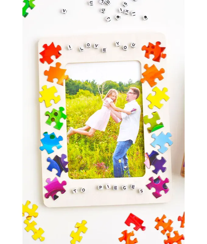 mothers-day-crafts: A white picture frame decorated with rainbow colored puzzle pieces in front of a white background. There are stray pieces next to the frame.' title='45 Mother’s Day Crafts for Kids That She’ll Actually Want to Keep