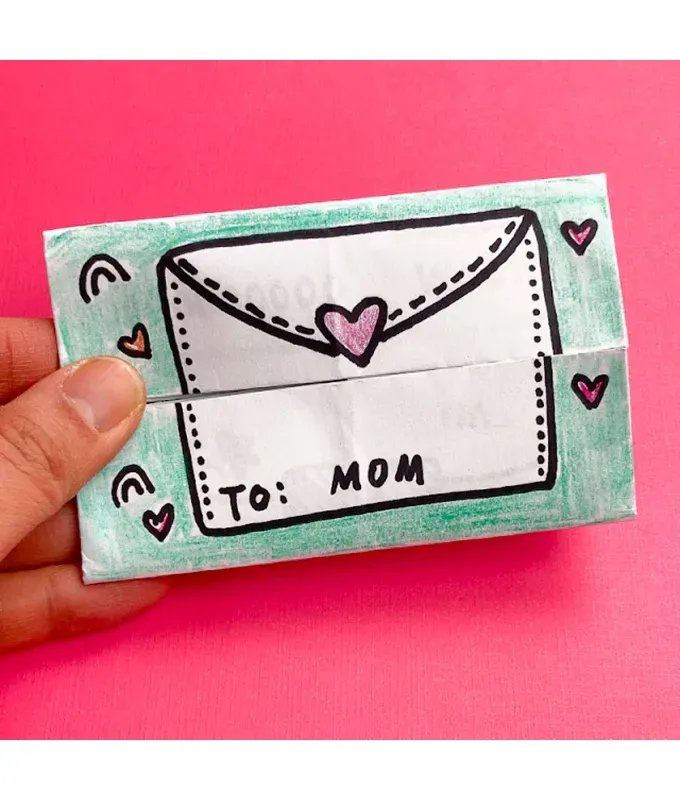 mothers-day-crafts: A papercraft origami in the shape of an envelope that says ’To: Mom’ in front of a pink background.' title='45 Mother’s Day Crafts for Kids That She’ll Actually Want to Keep