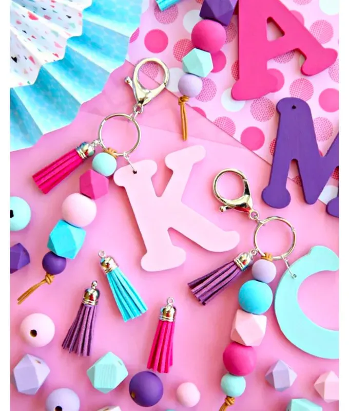 mothers-day-crafts: Colorful wooden keychains in the shape of letters with beads and tassles in front of a pink background.' title='45 Mother’s Day Crafts for Kids That She’ll Actually Want to Keep