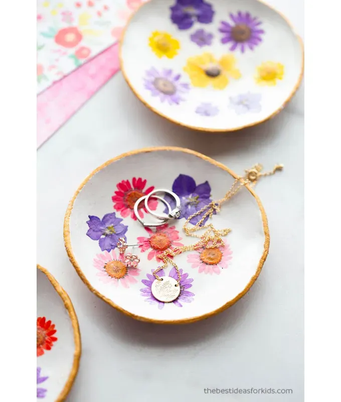 mothers-day-crafts: A clay dish with pressed flowers and a gold rim filled with rings and necklace. There are two other similar bowls in the frame.' title='45 Mother’s Day Crafts for Kids That She’ll Actually Want to Keep