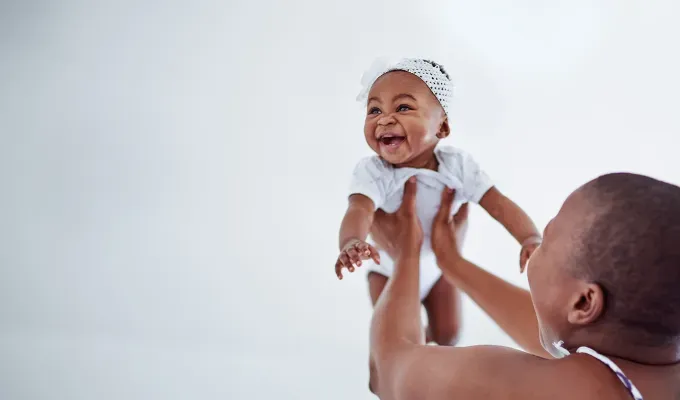 names-that-mean-fire: a baby girl smiling while being held in the air.' fetchpriority='auto' title='100 Baby Names That Mean Fire Perfect for the Formidable Bun in Your Oven