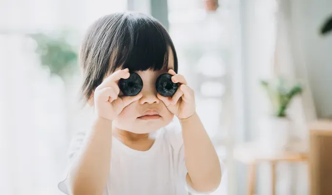 names-that-mean-fire: a young girl holding blueberries on her eyes.' fetchpriority='auto' title='100 Baby Names That Mean Fire Perfect for the Formidable Bun in Your Oven