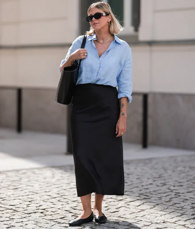 woman wearing a black midi skirt and blue shirt' fetchpriority='auto' title='22 Easy Black Skirt Outfit Ideas for When You Have Five Minutes to Get Dressed