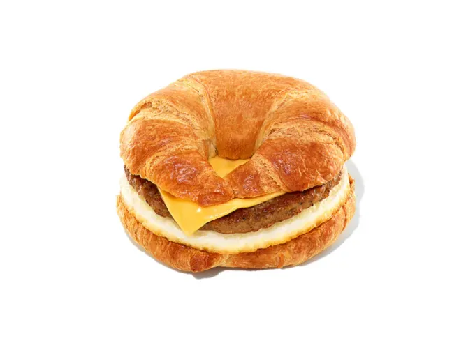 Keto at Dunkin Donuts - A croissant with sausage egg and cheese inside of it from Dunkin in front of a white background.' title='How to Eat Keto at Dunkin’ Donuts: 15 Low-Carb Foods and Drinks We Love