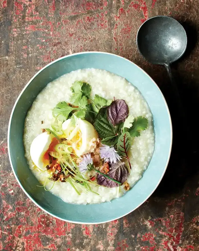 traditional chinese foods: bowl of congee topped with soft-boiled egg and greens' title='20 Traditional Chinese Food Dishes You Need to Try According to a Chinese-Malaysian Chef