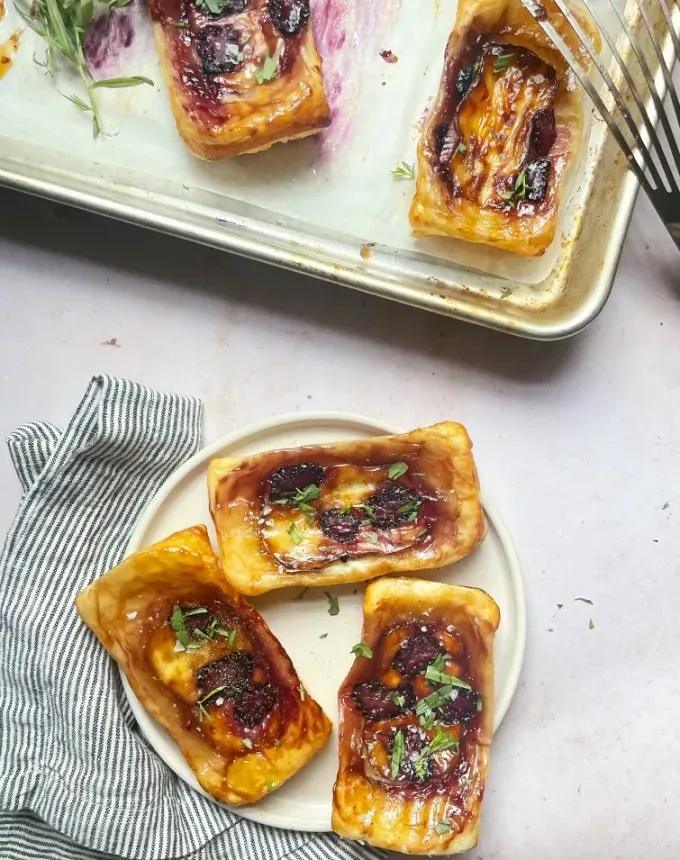 brie recipes: three blackberry-brie upside-down pastries on a plate with more on a baking sheet next to them' title='The 43 Most Delicious Brie Recipes That Put the Cheese Front and Center