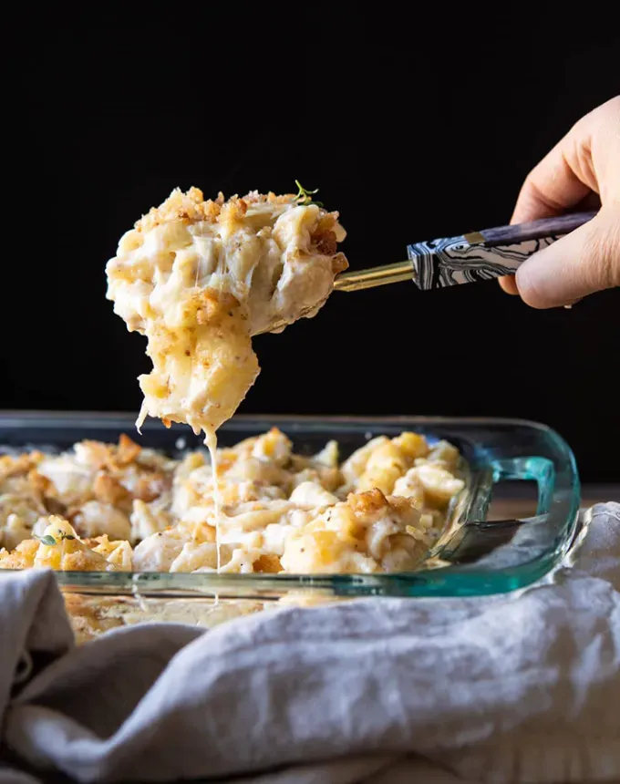 brie recipes: baked brie mac and cheese with a person lifting a scoop of the dish' title='The 43 Most Delicious Brie Recipes That Put the Cheese Front and Center
