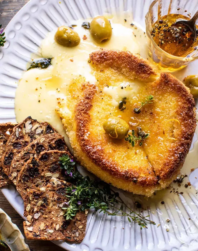 brie recipes: wheel of pan-friend golden brown brie topped with peppered honey olives and crackers' title='The 43 Most Delicious Brie Recipes That Put the Cheese Front and Center