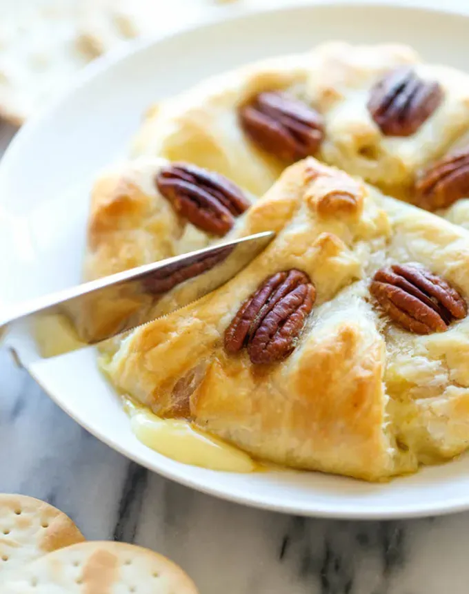 brie recipes: close-up of a knife cutting through a pumpkin-pecan wheel of brie' title='The 43 Most Delicious Brie Recipes That Put the Cheese Front and Center