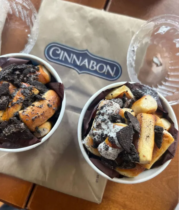 auntie-annies-cinnabon-oreo-topped-nuggets-and-buns: An overhead shot of Auntie Anne’s OREO topped pretzel nuggets and a Cinnabon paper bag.' fetchpriority='auto' title='Auntie Anne’s Cinnabon & Oreo United for the Ultimate Sweet Treat Collab and I Taste-Tested It Just for You