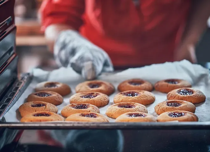 how to keep cookies soft: person checking on a tray of thumbprint cookies in the oven' fetchpriority='auto' title='How to Keep Cookies Soft So They Taste Fresh for Days