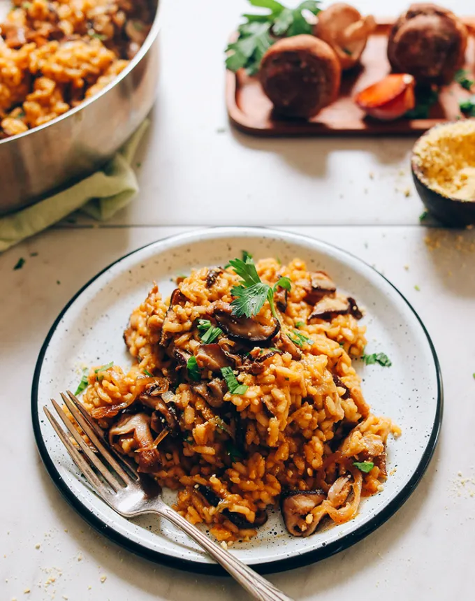best big-batch recipes: caramelized shiitake mushroom risotto on a plate with vegetables and a baking dish of the risotto in the background' title='76 Big-Batch Dishes & Recipes to Feed a Crowd
