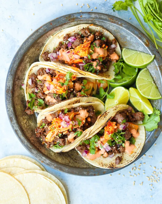 best big-batch recipes: four korean beef tacos on a plate with lime wedges' title='76 Big-Batch Dishes & Recipes to Feed a Crowd