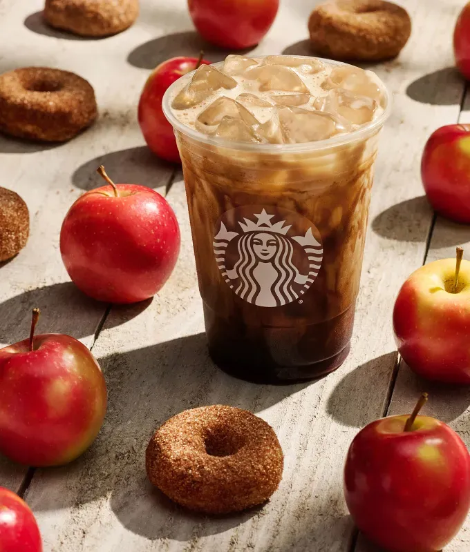 best starbucks fall drinks: starbucks apple crisp oatmilk shaken espresso surrounded by apples and apple cider doughnuts' fetchpriority='auto' title='The Best Starbucks Fall Drinks to Order in 2025 According to a Former Barista (Including a New Nutty Bev You’ll Love)