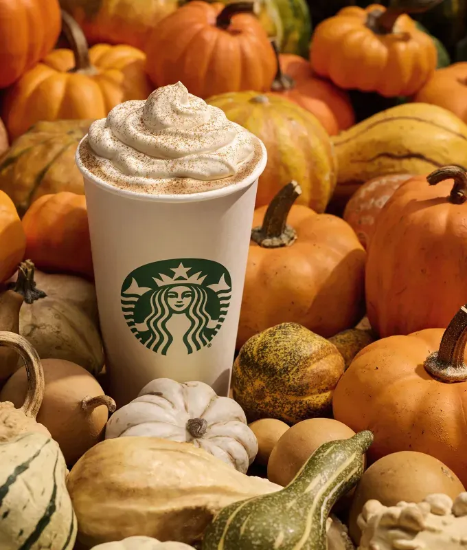 starbucks pumpkin spice latte returns: starbucks pumpkin spice latte surrounded by pumpkins and gourds' fetchpriority='auto' title='The Starbucks Pumpkin Spice Latte Is Back in August (& Its Early Return Is a Sign of the Times)