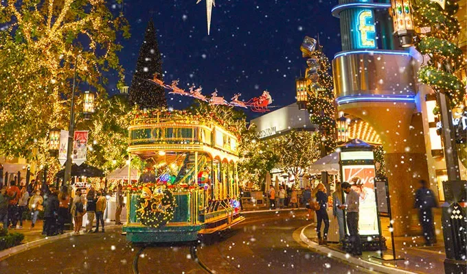 Where to See Christmas Lights L.A. - A green trolley wrapped in string lights and decorated for the holidays drives down The Grove which is decorated with festive lights and other holiday motifs.' title='Where to See Festive Christmas Lights in Los Angeles This Year (Including Drive-Thrus)