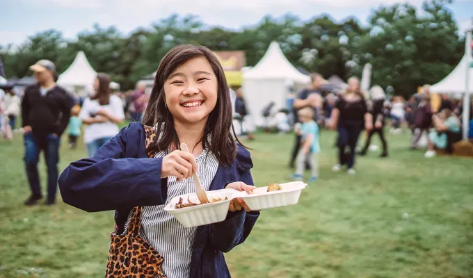 things-to-do-on-a-sunday-in-nyc: a young girl eating at smorgasburg.' title='18 Things to Do on a Sunday in NYC That Are Anything But Boring